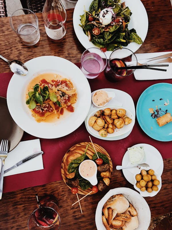 Overhead view of a shared restaurant table with pasta, salad, bread and small plates